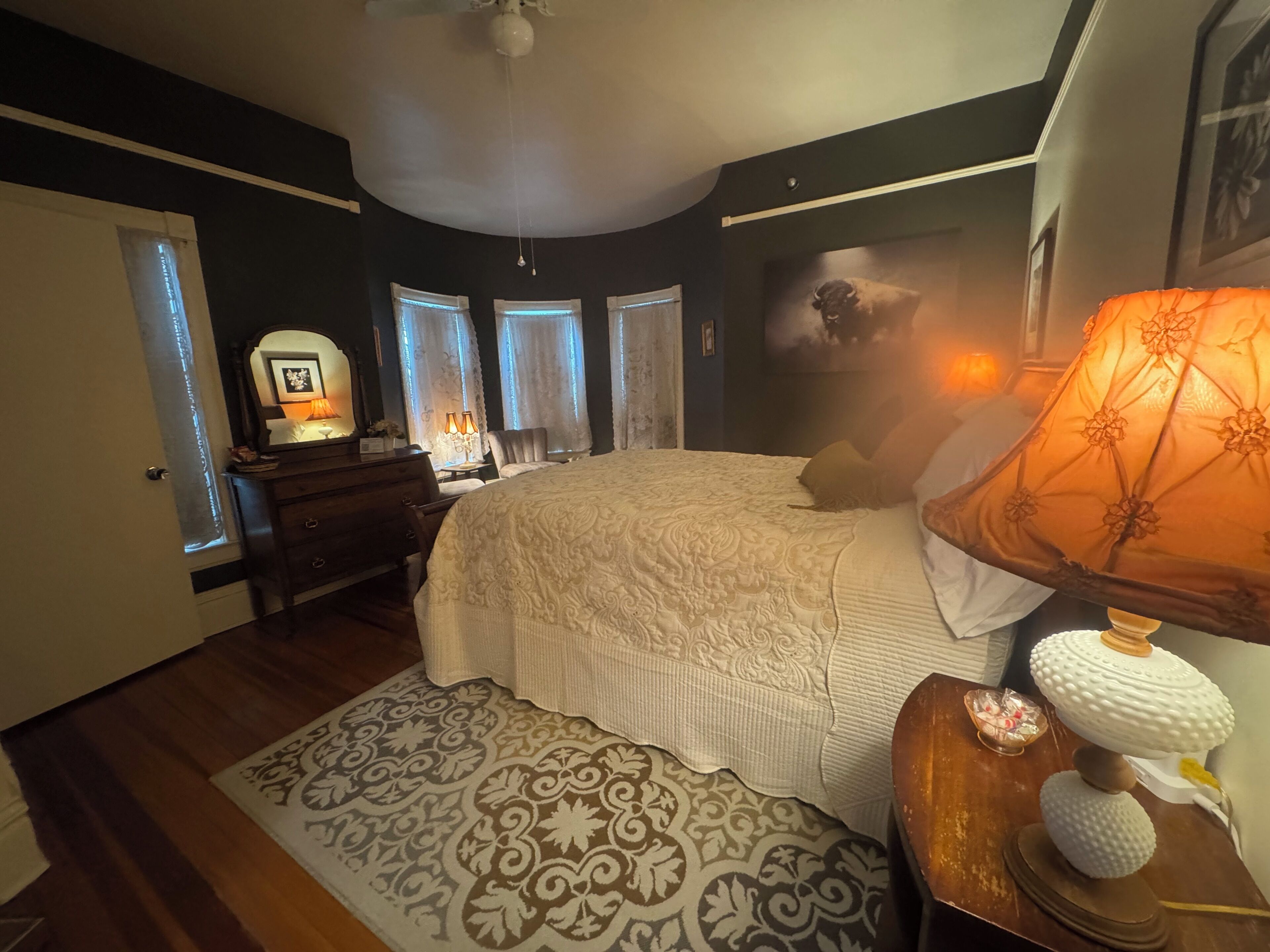 A bedroom with a bed, dresser, bedside lamps, and a patterned rug.