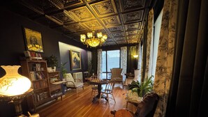 A room with a wooden floor, a chandelier, a bookshelf, a chessboard, and a window with curtains. - The Boho Buffalo Inn (Buffalo)