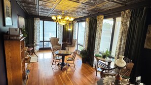 A room with a wooden floor, a chandelier, a chessboard, and a view through large windows. - The Boho Buffalo Inn (Buffalo)
