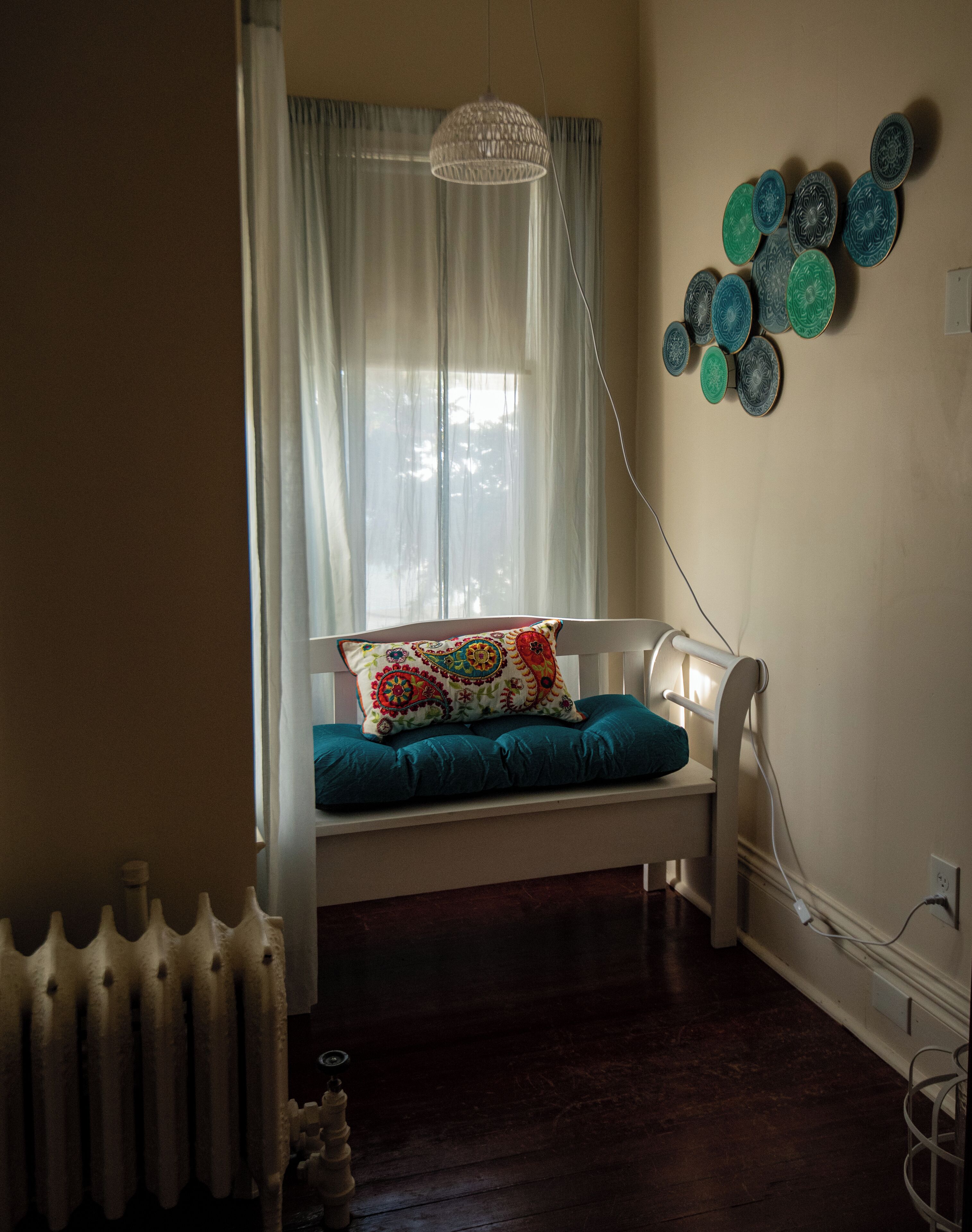 A cozy room with a white bench, a patterned cushion, a hanging light fixture, and decorative plates on the wall.