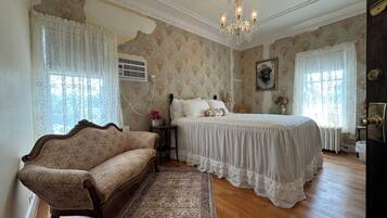 A bedroom with a bed, a sofa, a chandelier, floral wallpaper, and a ceiling with decorative moldings.