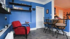 Ein Zimmer mit blauen Wänden, einem roten Sessel, einem Esstisch mit Stühlen und einer weißen Heizung.