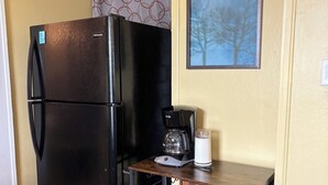 Eine kleine Küchenzeile mit einem schwarzen Kühlschrank, einer Kaffeemaschine und einem kleinen Holzschrank.