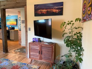 Una sala de estar con televisor de pantalla plana, un mueble de madera, una planta en maceta y una pintura con vista a la ciudad.