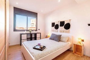 A bedroom with a bed, bedside tables, a window, and a view of buildings. - City • Penthouse - Unik Vacation (Tarragona)