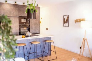 A modern kitchen with a central island, bar stools, and a tripod lamp. - City • Penthouse - Unik Vacation (Tarragona)