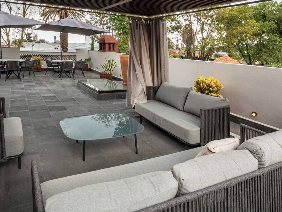 Une terrasse extérieure avec un canapé, des fauteuils, une table en verre et des parasols.