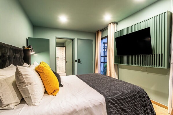 A modern hotel room with a large bed, a flat-screen TV mounted on the wall, and a door leading to a balcony. - Casa Juárez (Puebla)
