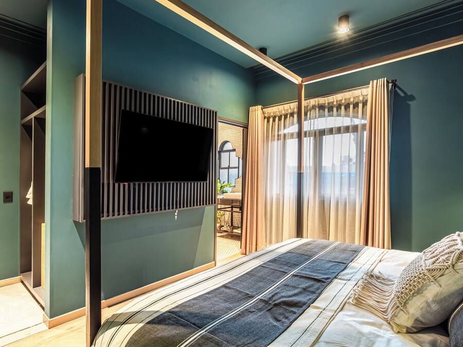 Un dormitorio con cama, televisor montado en la pared y ventana con cortinas.
