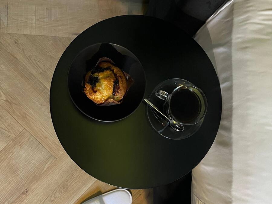 Una mesa redonda con un plato de comida y una taza de café, zapatillas blancas y suelo de madera.