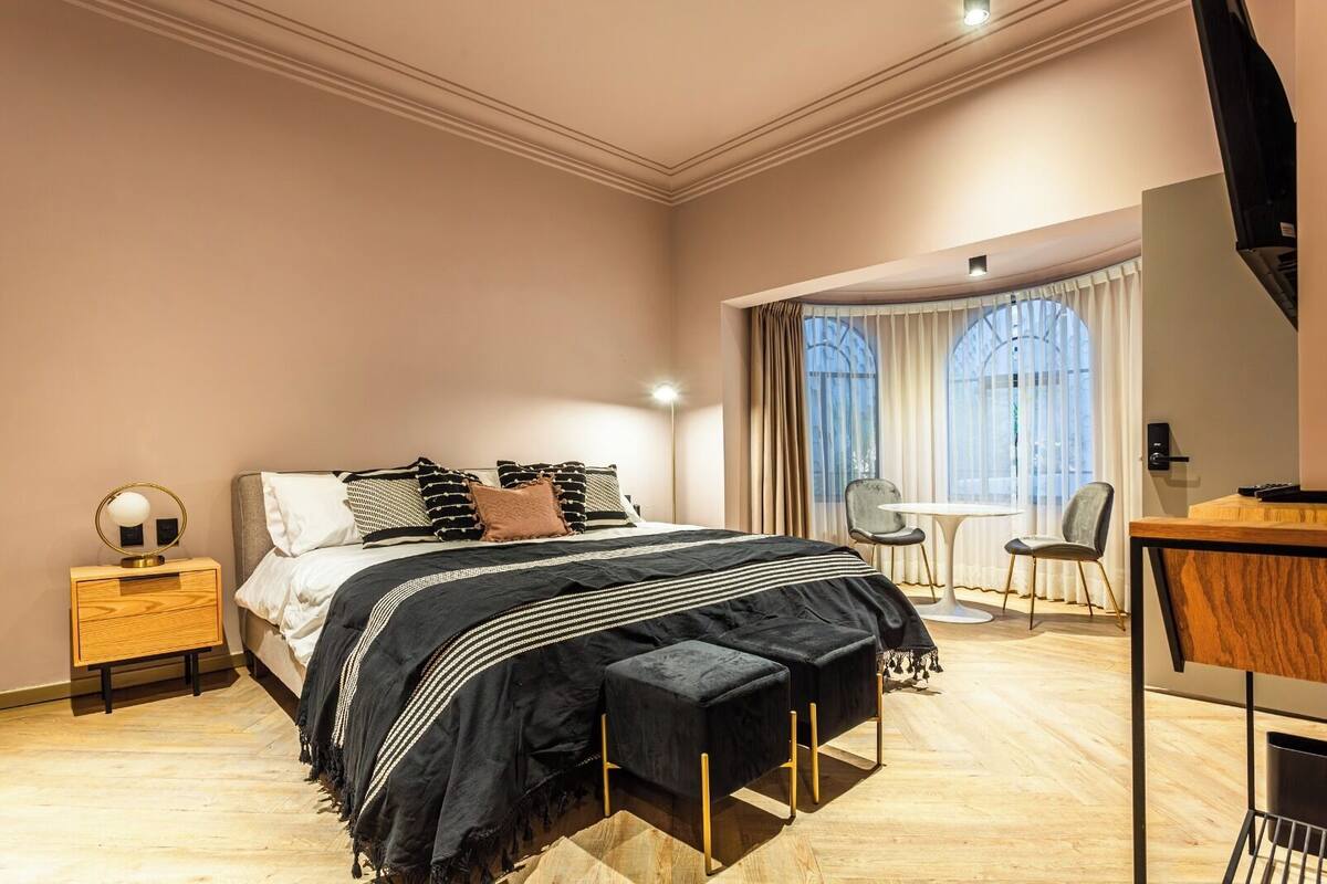 A modern bedroom with a large bed, bedside table, and a desk area with a chair.