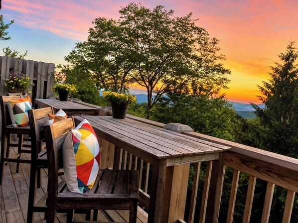 An outdoor deck with wooden furniture and potted plants, overlooking a scenic view.