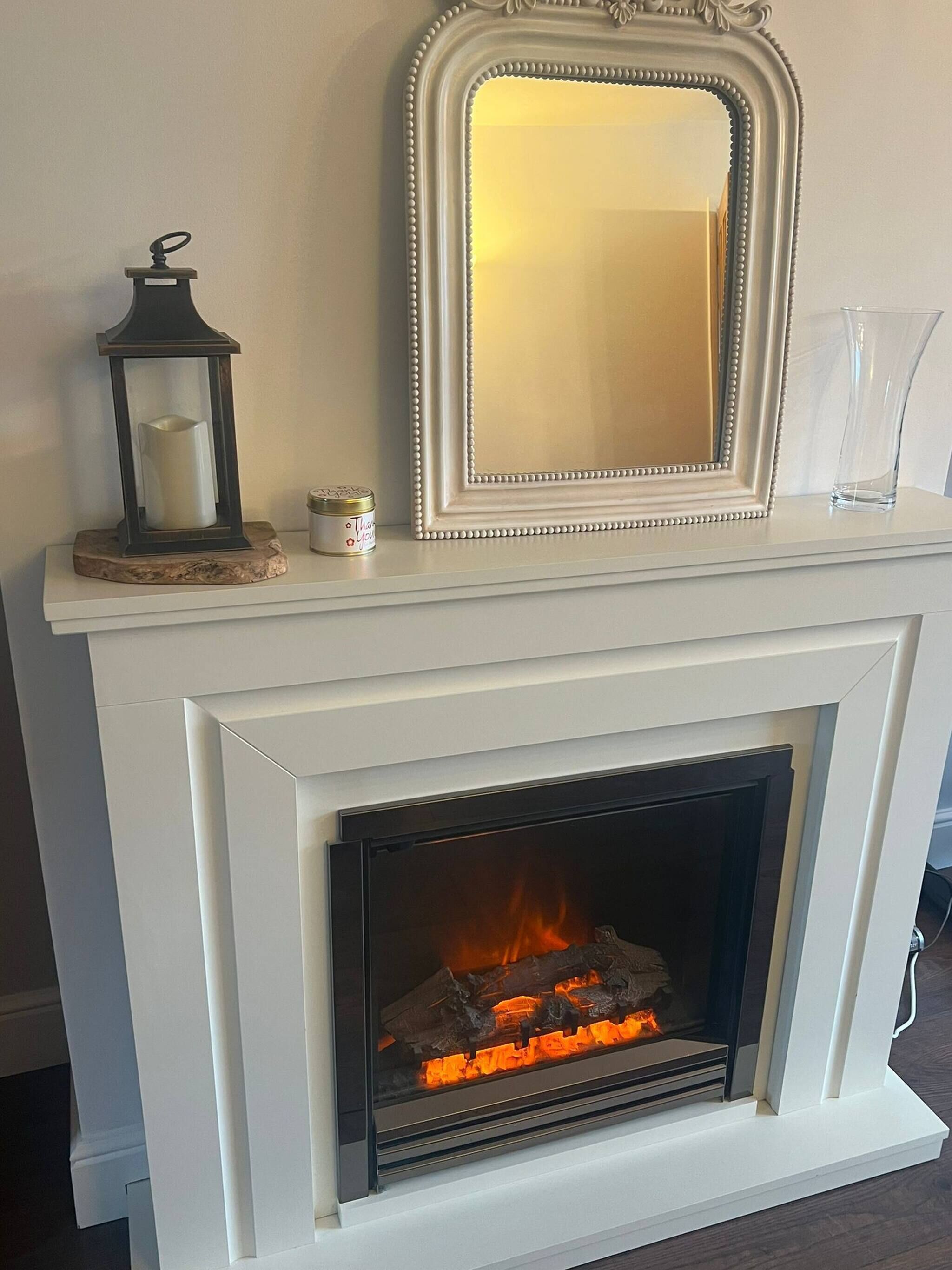 A fireplace with a white mantel, a mirror, a candle, and a glass vase.