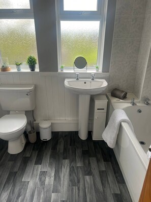 A bathroom with a toilet, sink, and bathtub, wooden flooring, and a window with a view of greenery. - Comfortable 3 Bedroom House-ng5,sleeps 5 (Nottingham)