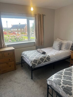 A bedroom with a bed, a dresser, a window with curtains, and a radiator. - Comfortable 3 Bedroom House-ng5,sleeps 5 (Nottingham)