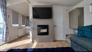 Una sala moderna con un televisor de pantalla plana montado en la pared, una chimenea empotrada, un tapete azul y un sofá gris.