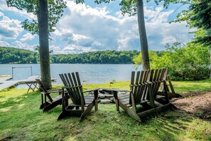 Due poltrone Adirondack rivolte verso un lago con un pontile e un piccolo fuoco.