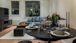 Een moderne woonkamer met een eettafel gedekt voor een maaltijd, een bank met opvallende kussens, en een televisie op de achtergrond.
