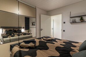 Une chambre à coucher avec un lit, un miroir, une porte et une étagère sur laquelle sont posés divers objets.