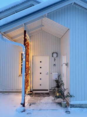 L’extérieur d’un bâtiment est recouvert de neige. On y voit une porte blanche, une petite fenêtre et une boîte aux lettres.