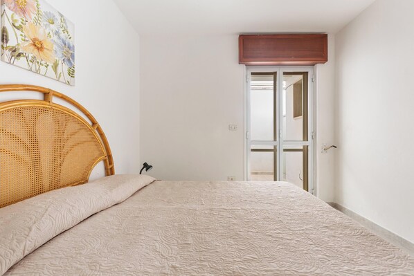 Un dormitorio con cama, cabecera de madera, una puerta y un cuadro colgado en la pared.