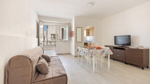 A living room with a sofa, a dining table with chairs, a TV, and a cabinet.