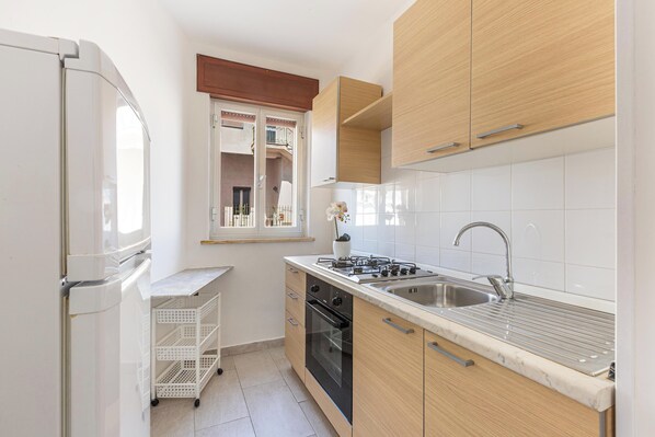 Una cocina compacta con gabinetes blancos, un lavamanos de acero inoxidable, una estufa y una ventana pequeña con vistas.
