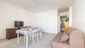 A compact living space with a dining area, a sofa, a TV, and a kitchenette.