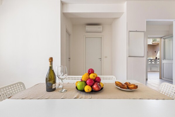 Een eethoek met een tafel gedekt voor twee personen, met een fruitschaal, een fles wijn en een bord gebak.