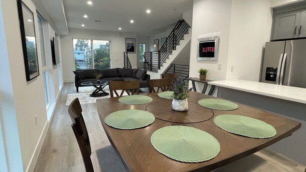 Una cocina moderna con comedor, que incluye una mesa de madera con individuales verdes, una estufa empotrada y un refrigerador de acero inoxidable.