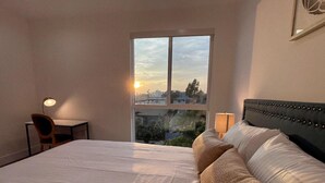 Habitación de hotel con una cama grande, un escritorio y una silla. Se ve una ventana con vistas a edificios y árboles.