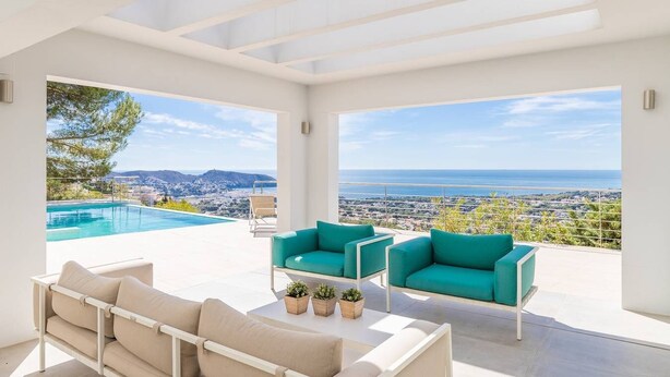 A modern outdoor living space with a pool, two teal armchairs, a beige sofa, and a view of the sea and city. - Villa met Zeezicht, Wifi en Airconditioning (Moraira)