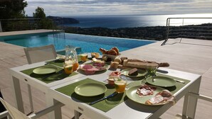 A dining table set with plates, cutlery, and a pitcher of juice, overlooking a pool and ocean view. - Villa met Zeezicht, Wifi en Airconditioning (Moraira)
