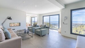 A modern living room with a sofa, armchairs, a coffee table, and a TV. There are large windows with a view of the city. - Villa met Zeezicht, Wifi en Airconditioning (Moraira)