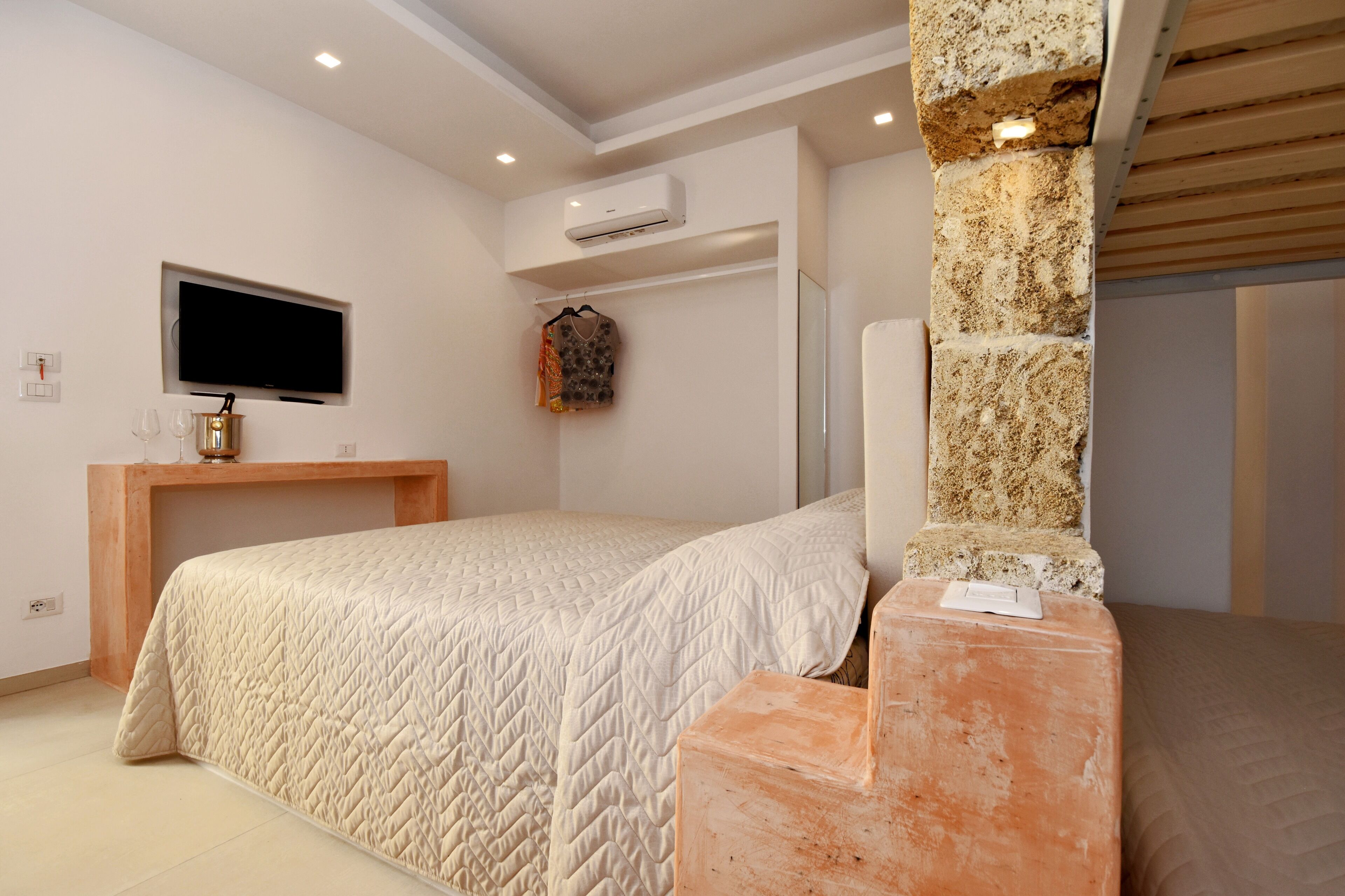 A bedroom with a bed, a TV mounted on the wall, and an air conditioning unit.