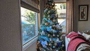 Een gezellige woonkamer met een groot raam, een houten vloer, een beige bank en een versierde kerstboom.