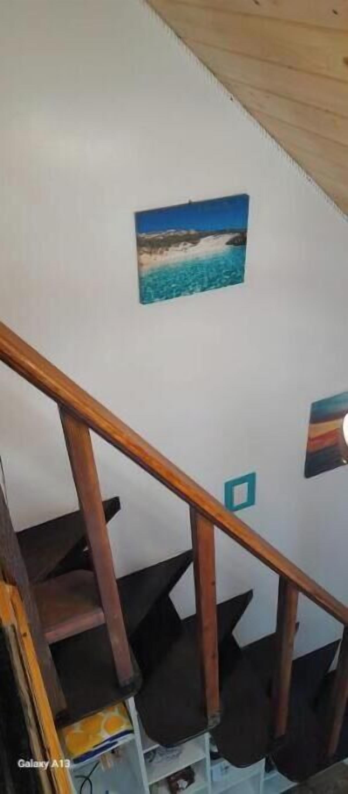 A staircase with wooden handrails and a small painting of a beach scene on the wall.