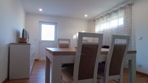 A dining area with a white table and chairs, a small refrigerator, and a window with a view. - Mondalva Apartments located in village of Quintela, near to São Pedro de Alva (São Pedro de Alva)