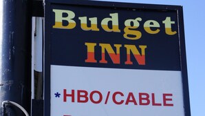 Placa do Budget Inn listando comodidades como HBO/TV a cabo, telefones de discagem direta, cozinha compacta e tarifas diárias.