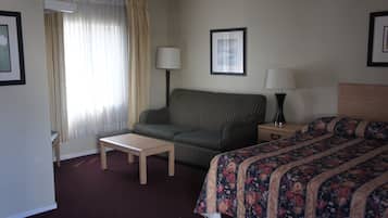 A hotel room with a striped sofa, a bed with a floral bedspread, a small table, two bedside lamps, and a window with curtains.