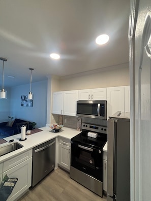 Kitchen features a sink, microwave, oven, refrigerator, and countertop with a bowl of snacks.