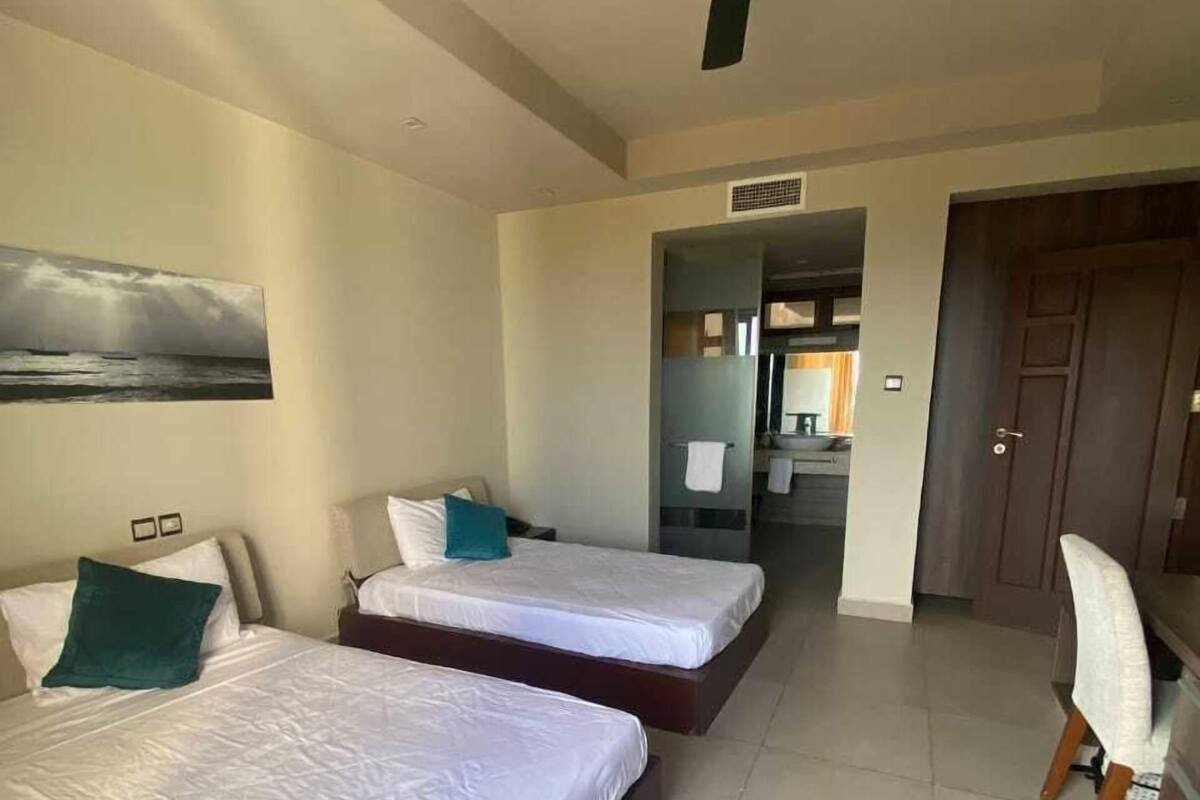 Ein Hotelzimmer mit zwei Betten, einem Deckenventilator, einem Gemälde an der Wand und Blick ins Bad.