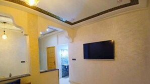 Un couloir avec un canapé bleu, un téléviseur à écran plat fixé au mur et un mur en pierre en arrière-plan.
