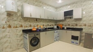 Une cuisine compacte avec des meubles blancs, un lave-linge encastré et un four à micro-ondes.