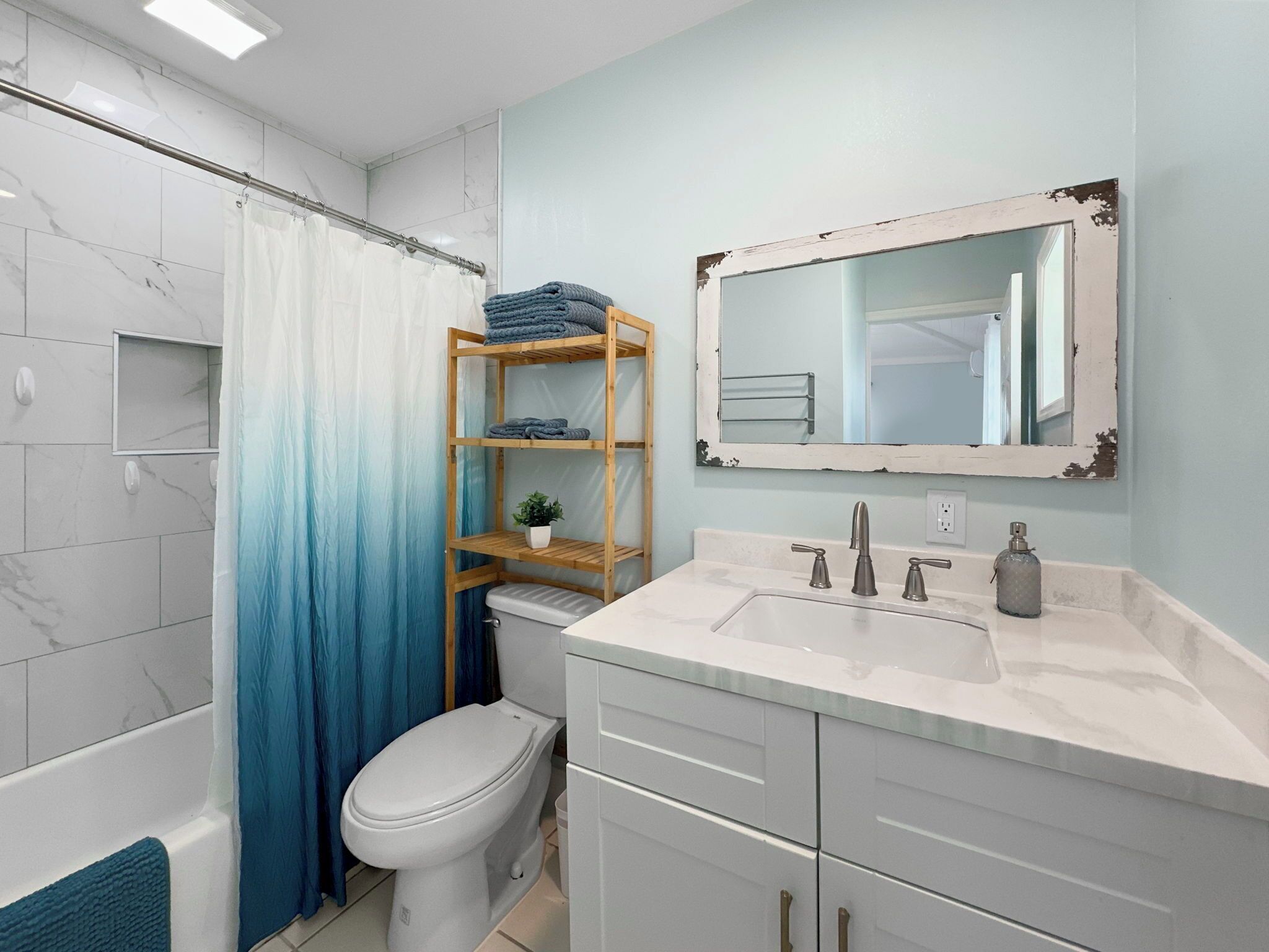 Un baño con un inodoro blanco, un estante de madera con toallas, un espejo y un lavabo con grifo.