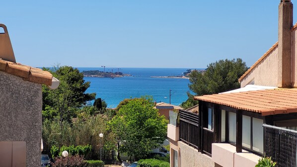 A coastal view with a clear sky, a distant construction site, and lush greenery.