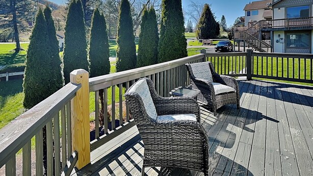 A wooden deck with wicker furniture, a railing, and a view of a residential area with houses and trees. - Ski Boots N' Bathing Suits by Taylor Made Deep Creek (McHenry)