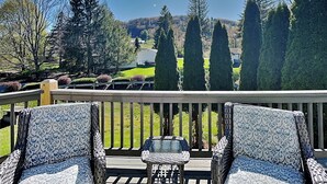 A deck with outdoor furniture, a view of a green landscape, and tall trees. - Ski Boots N' Bathing Suits by Taylor Made Deep Creek (McHenry)