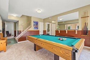 A pool table in a room with a wooden floor, a door, and a poster on the wall.