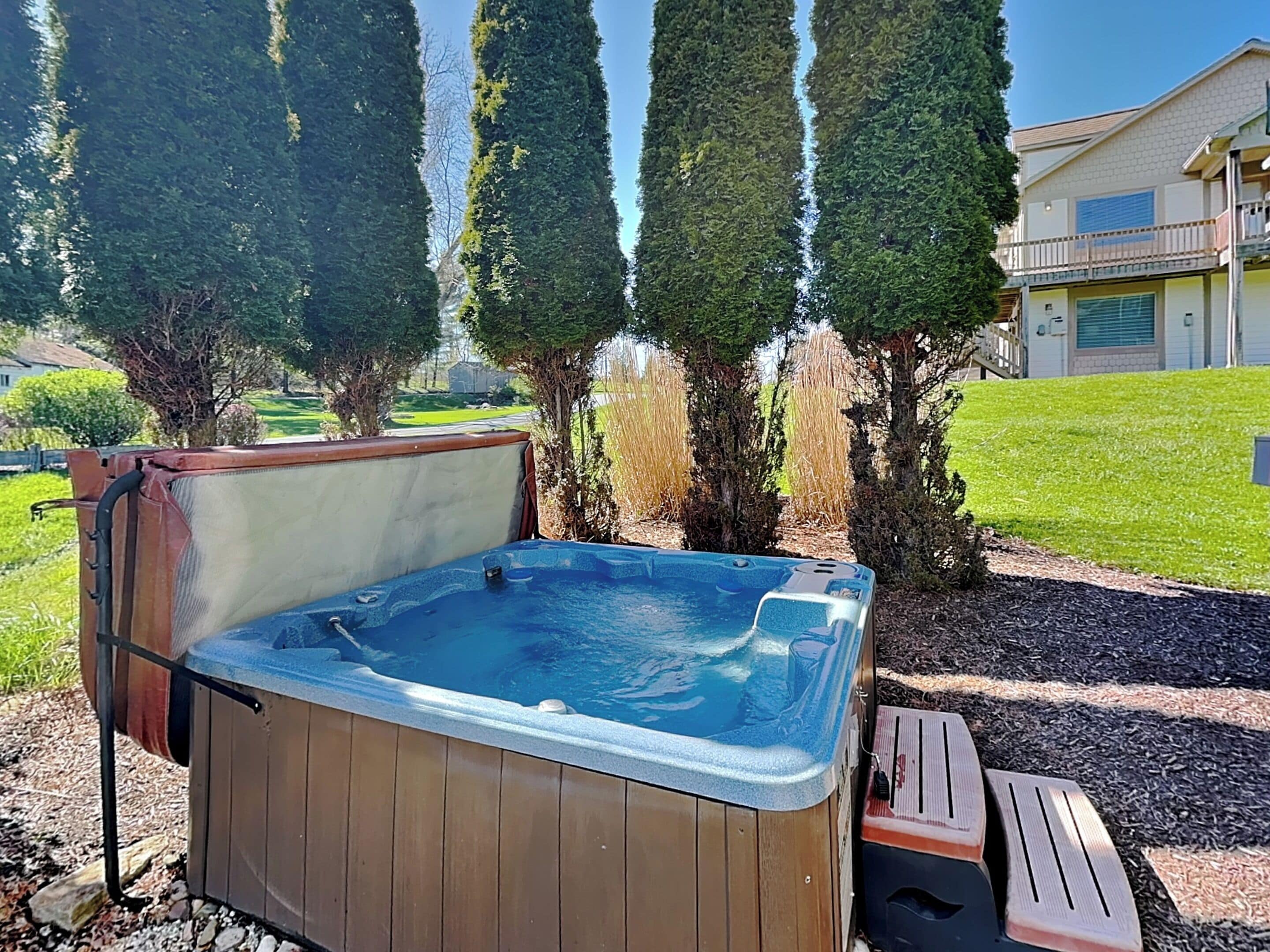 Un bain à remous avec une structure extérieure en bois, entouré d’une pelouse et de grands arbres.